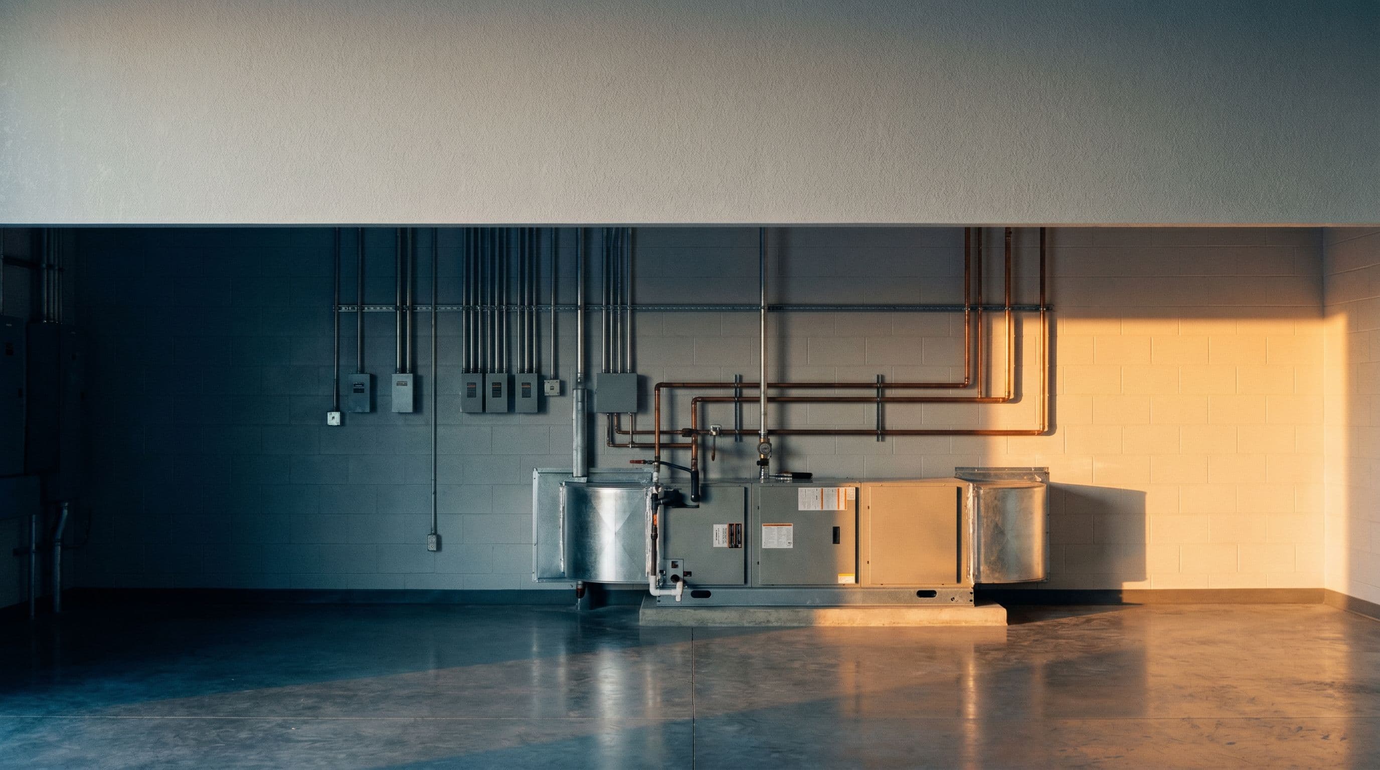 Commercial mechanical room with electrical conduit, copper plumbing risers, and an air handler. Orderly, well-maintained.